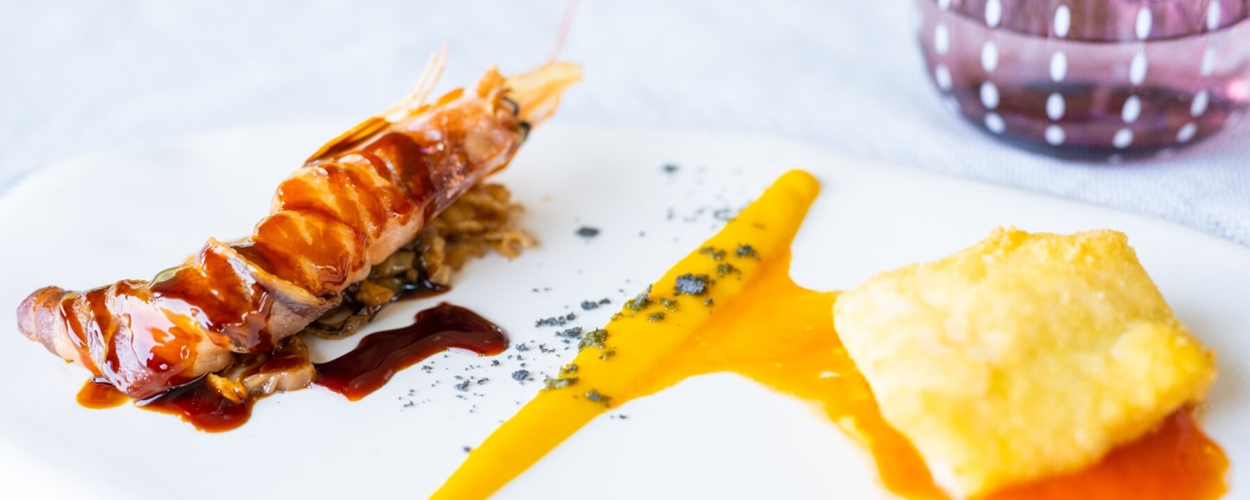 Gambero con salsa scura su cipolle fritte, spruzzi di salsa giallo-arancio e un cibo fritto in un'atmosfera da ristorante.