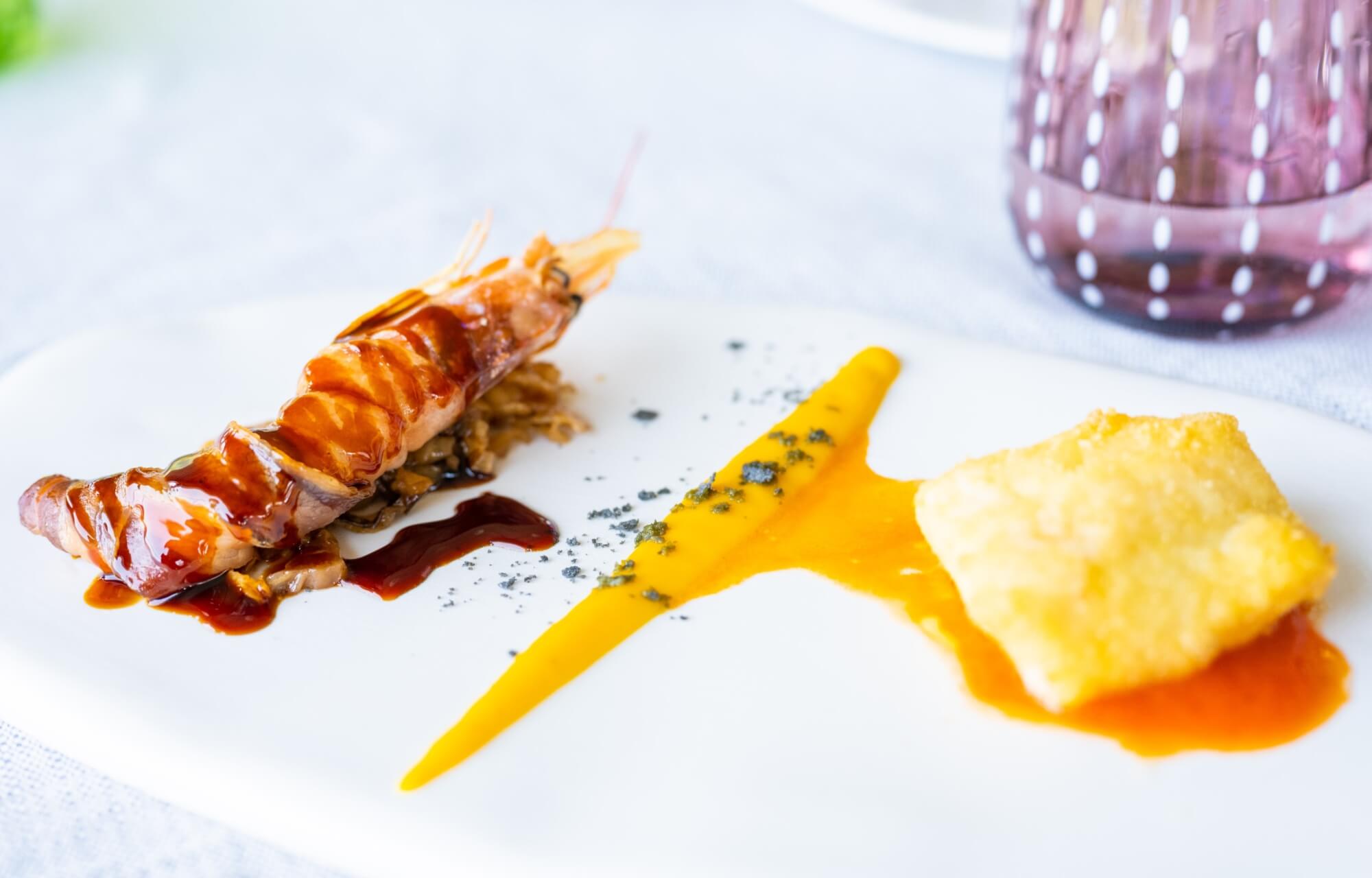 Piatto elegante con gambero, decorato con salsa gialla, in un ambiente di ristorazione formale.