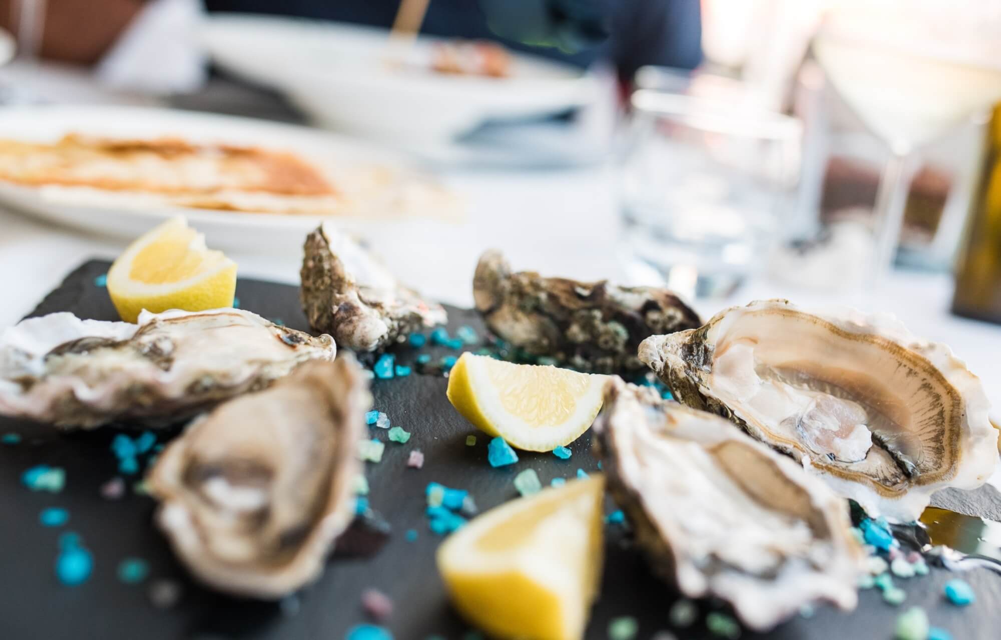 Piatto di ostriche con limoni su superficie scura, decorato con guarnizioni blu e verdi, in un ambiente di ristorazione.