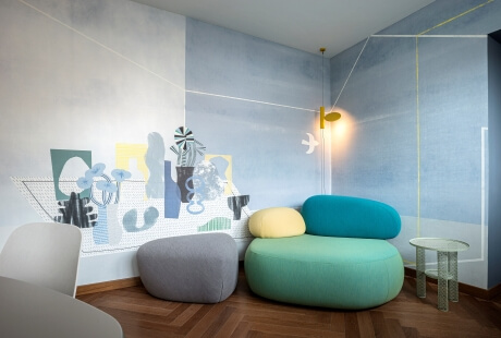 Una stanza moderna e minimalista con un divano multicolore, ottomani, un tavolo in vetro e un murale vibrante.