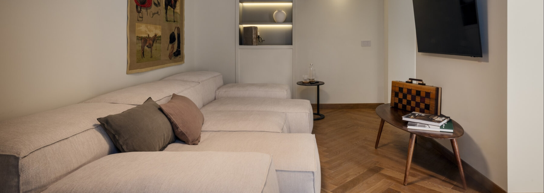 Cozy living room with a white couch, coffee table, and TV, featuring warm lighting and decorative items on shelves.