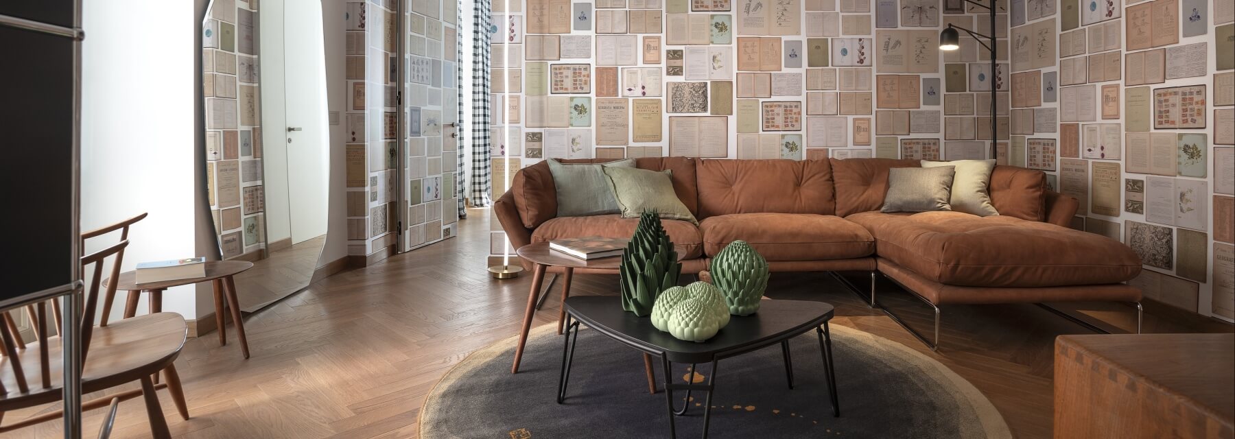 A modern living room with a collage of book covers, tan leather sofa, round coffee table, and warm lighting.