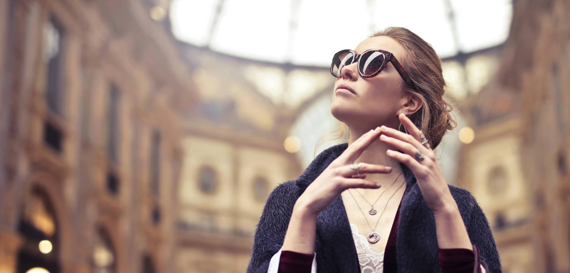Una donna con un cardigan blu scuro guarda il cielo, in piedi davanti a un edificio sfocato con un tetto a cupola.