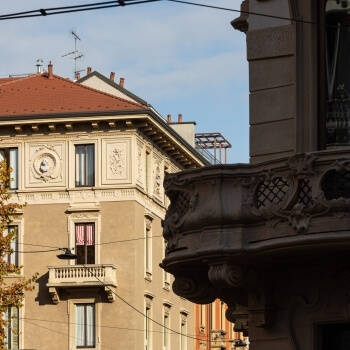 Due edifici in un contesto urbano, uno con dettagli ornamentali e un tetto in tegole rosse, l'altro parzialmente nascosto.