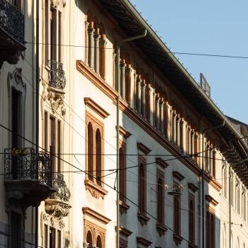 Edificio multi-piano con facciata crema e dettagli marroni, finestre ad arco, balcone in ferro e cielo blu sullo sfondo.