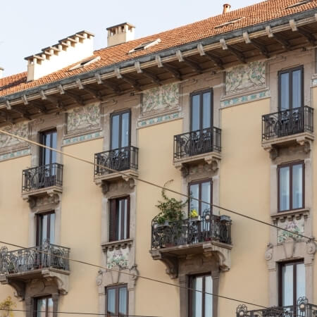 Multi-story building with balconies, light exterior, ornate details, terracotta roof, surrounded by trees and power lines.