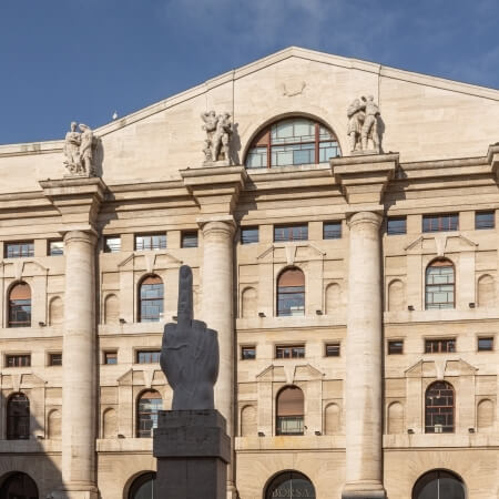 Grand tan building with triangular roof, six columns with statues, and a central finger sculpture against a blue sky.