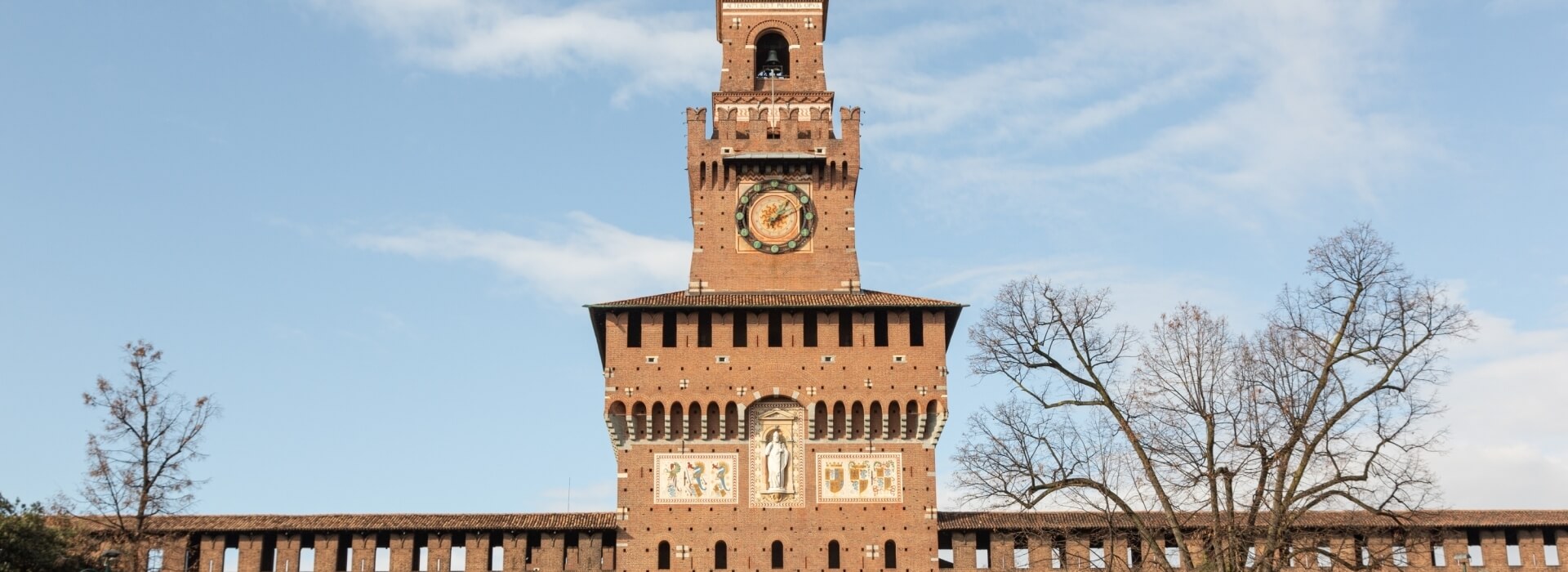 Torre storica in mattoni rossi con orologio, decorazioni e alberi, immersa in un'atmosfera di tranquillità.