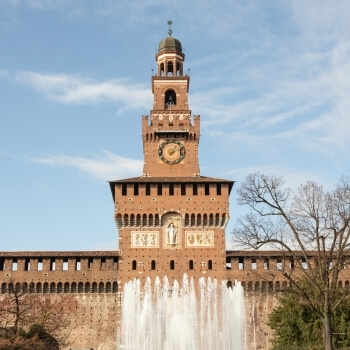 Castello Sforzesco con torre dell'orologio, fontana, albero spoglio e cielo sereno sullo sfondo.