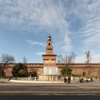 Museo con torre cilindrica, fontana, strada, alberi spogli e cielo blu con nuvole bianche nel cortile.