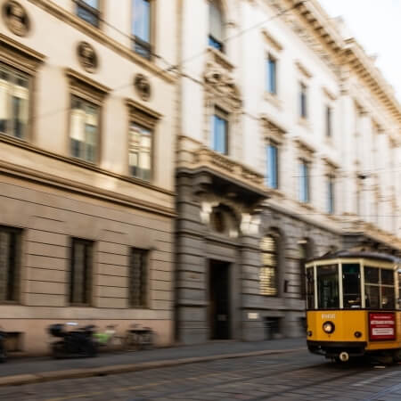 A yellow and white tram on a street, flanked by buildings of different eras, with a blurry, dynamic daytime atmosphere.