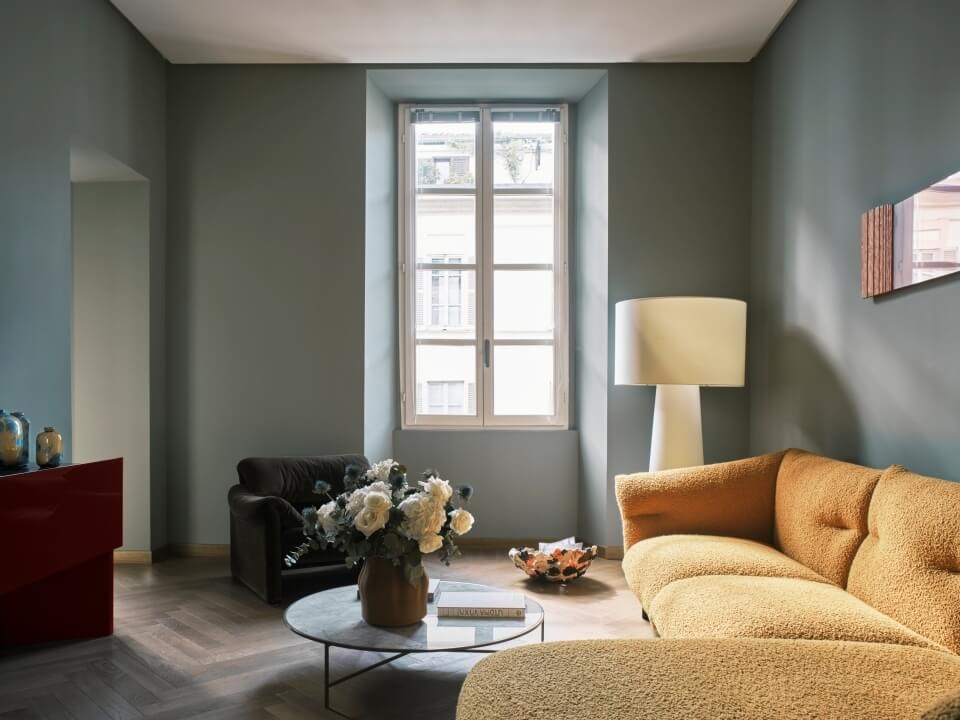 Cozy minimalist living room with a yellow couch, glass coffee table, and natural light from a large window.