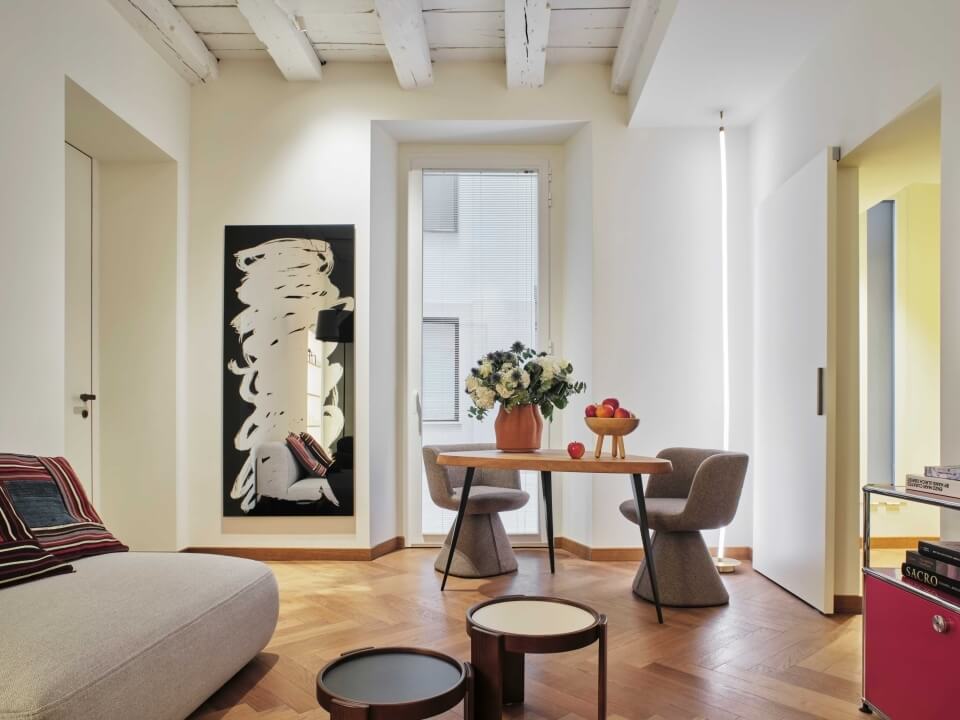 Soggiorno moderno minimalista con divano, tavoli, sedia, specchio e porte scorrevoli, illuminato da luce naturale.