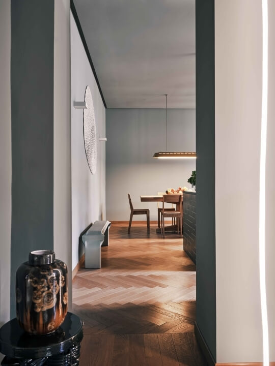 Interno minimalista moderno con area pranzo, corridoio, tavolo in legno, piante e decorazioni su pareti bianche.