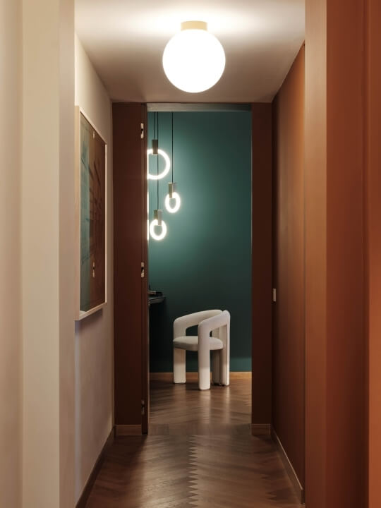 A dark hallway with wood floors, a white chair, a teal wall, and abstract artwork, creating a serene and elegant atmosphere.