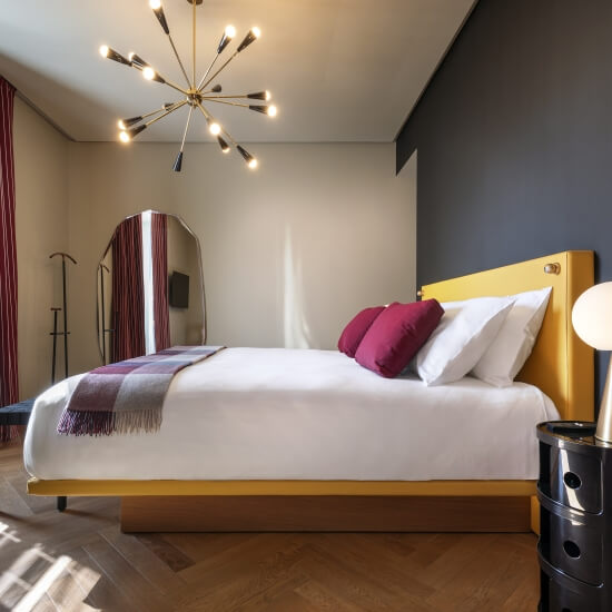 Camera elegante con letto con testiera dorata, specchio, lampade e un lampadario moderno. Pareti beige e grigie.