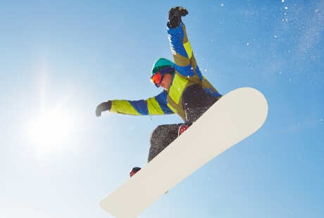 Snowboarder in mid-air against a blue sky, wearing colorful gear.   Snowboarder in volo contro un cielo blu, indossando abbigliamento colorato.