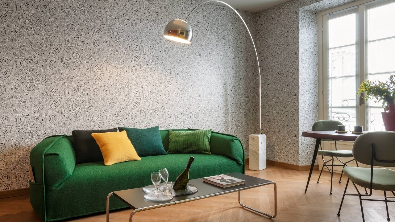 Modern living room with a green couch, coffee table, dining area, and natural light from windows, featuring minimalist decor.