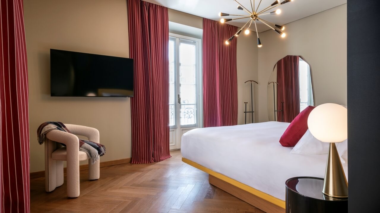 Elegant bedroom with a white bed, red curtains, stylish chair, and warm lighting, creating a serene and inviting atmosphere.