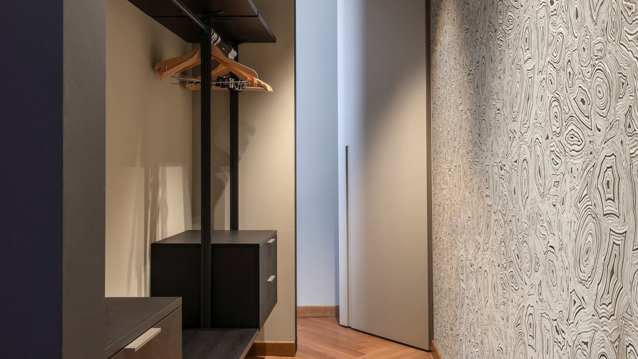 A compact closet with a black storage unit, wooden hangers, and a textured beige wall, set on a light wood floor.