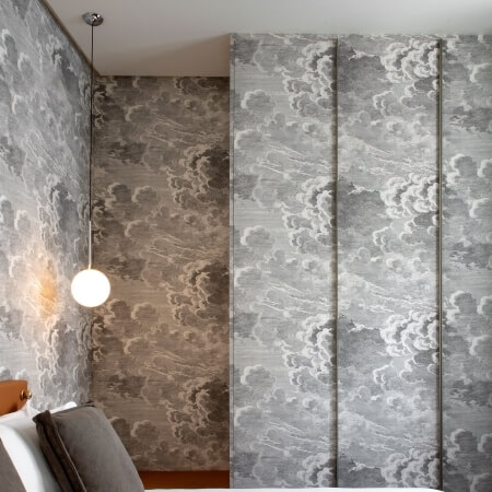 Serene hotel room with a cloud-pattern mural, cozy bed, and simple white light, creating a tranquil atmosphere.