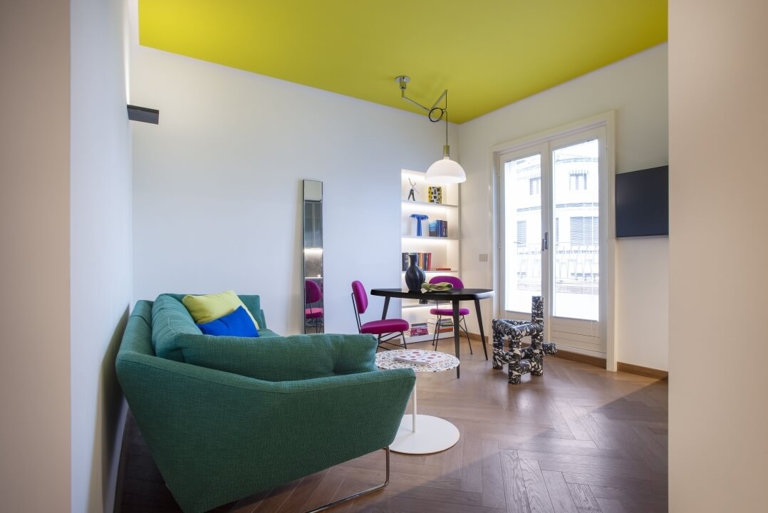 Soggiorno moderno con divano verde, tavolo nero, libreria, TV e porte scorrevoli, decorato con colori vivaci.