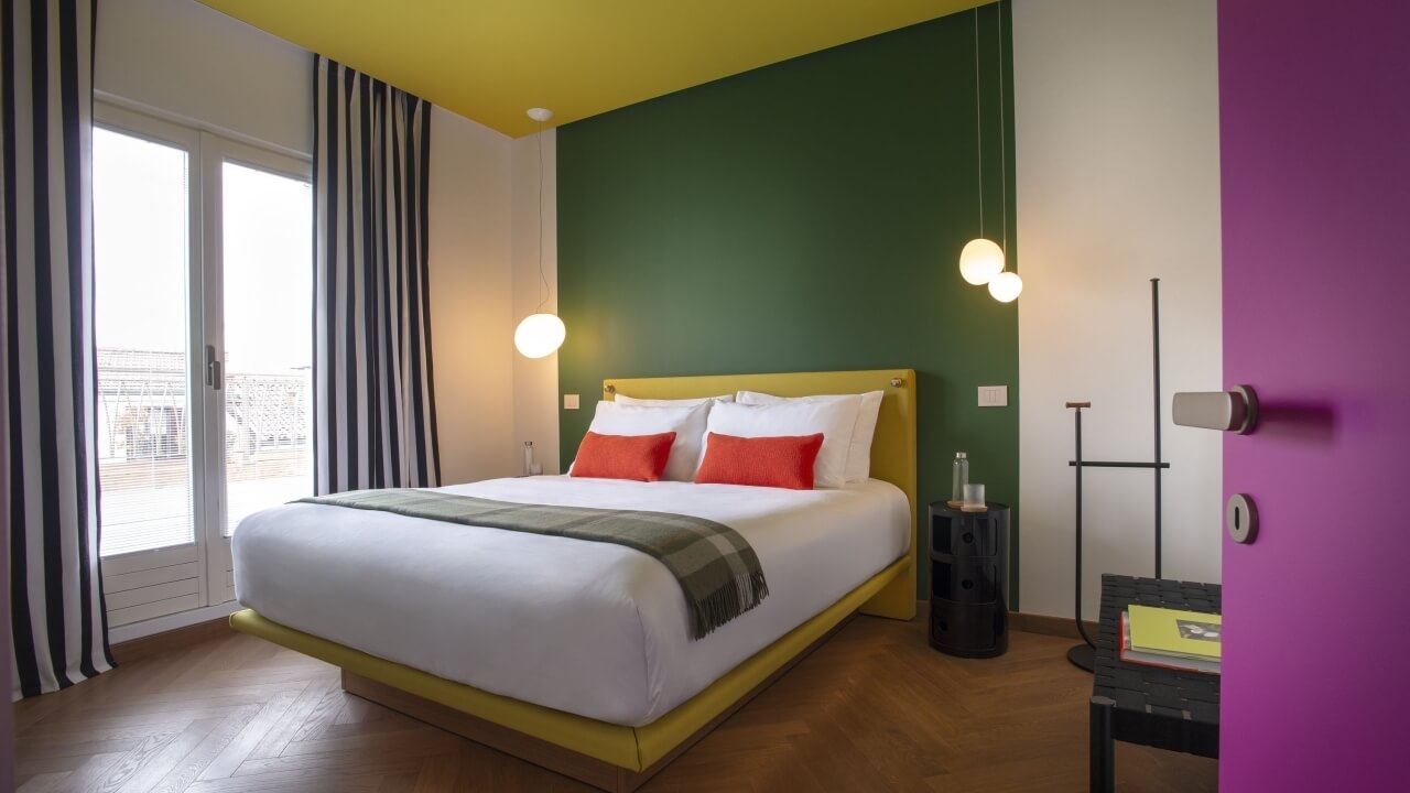 Modern bedroom with a green wall, large bed, nightstand, bench, and sliding glass door, featuring a minimalist design.