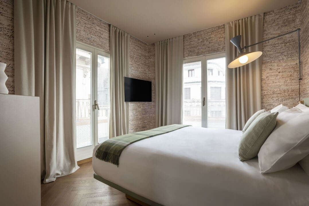 Camera da letto serena con letto grande, lenzuola bianche, pareti con scritte artistiche e luce naturale filtrante.