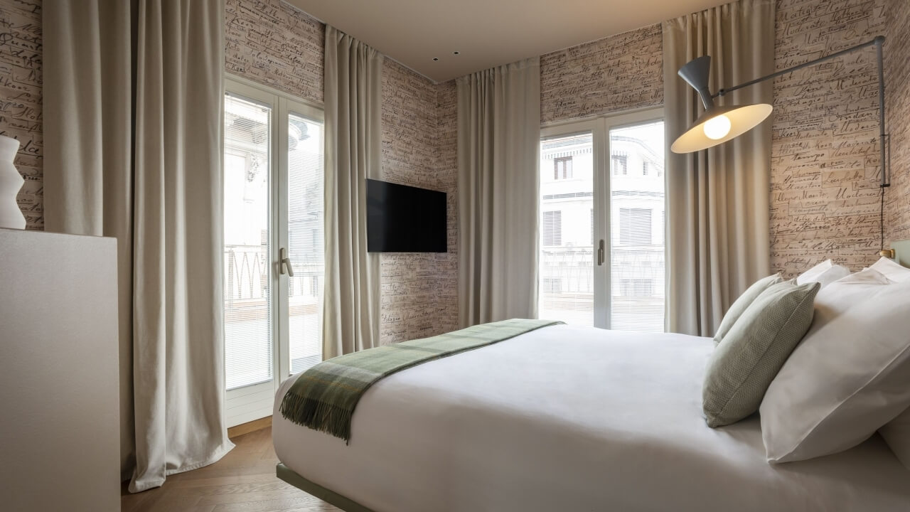 Serene bedroom with neutral decor, natural light, a wall-mounted TV, and vintage wallpaper, exuding calm and elegance.