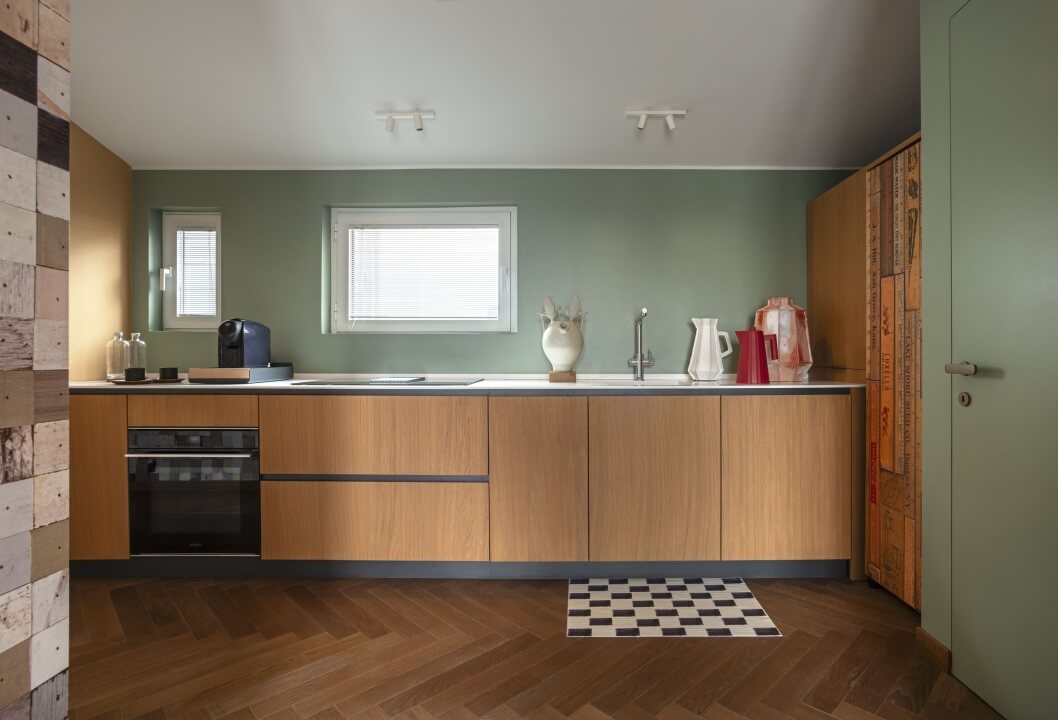 Cucina moderna con pareti verde chiaro, accenti in legno, illuminazione naturale, e un'atmosfera serena e sofisticata.