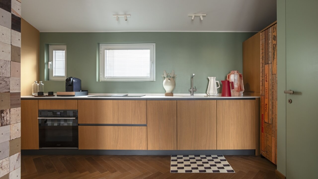 Modern kitchen with white countertop, wooden cabinets, black oven, sink, and checkered mat, featuring various kitchen items.