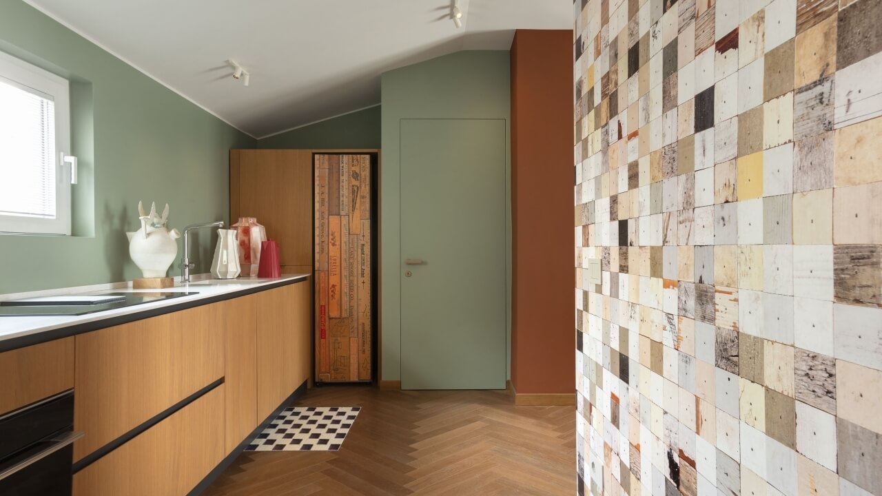 Cucina moderna ed eclettica con armadietti in legno chiaro, piano bianco, e porta verde che conduce a un'altra stanza.