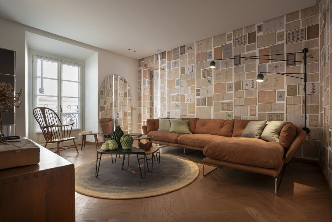 Soggiorno moderno con parete di documenti, divano marrone, poltrone, tavolino e luce naturale da una grande finestra.