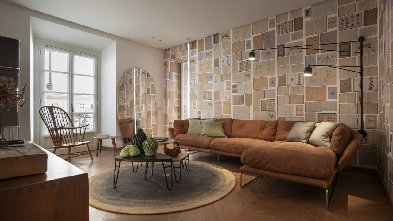 Modern living room with a brown leather couch, vintage book wallpaper, gray rug, and cozy decor elements.