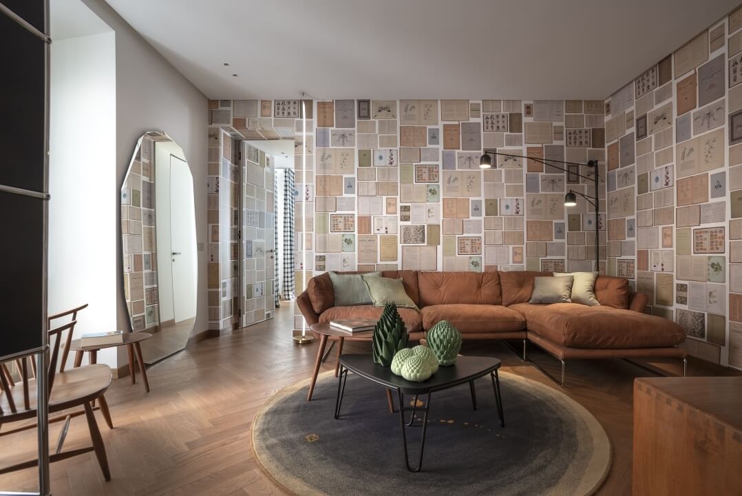 Soggiorno moderno ed eclettico con divano brown, pareti a mosaico, piante e decorazioni che creano un'atmosfera serena.
