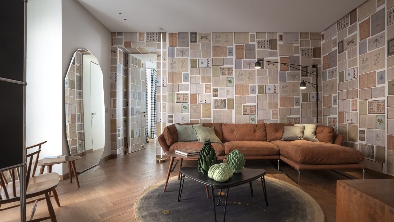 Modern living room with a unique wall collage, brown L-shaped couch, black coffee table, and colorful circular rug.