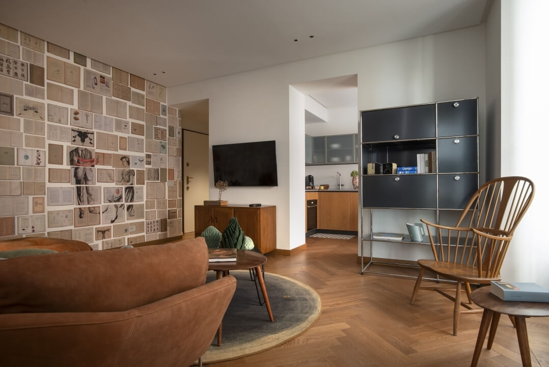 Salotto moderno con cucina in stile mid-century, pareti bianche e collage di immagini, divano in pelle marrone e mobili in legno.