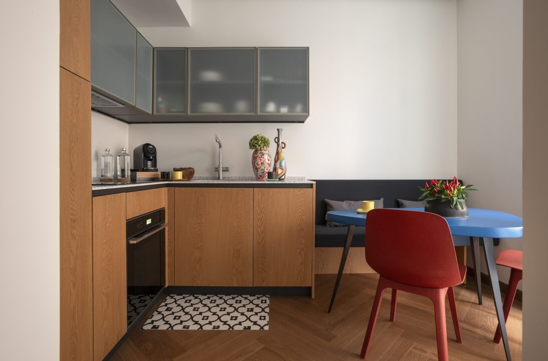 Cucina moderna con armadietti in legno, piano nero, angolo pranzo blu con sedie rosse, decor minimalista e piante.