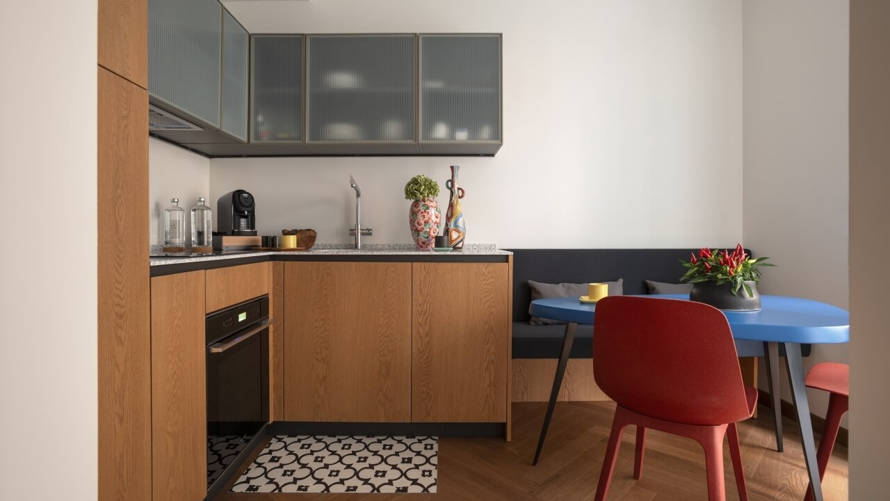 Modern kitchen and dining area with a blue table, red chairs, gray couch, and stylish countertop items.