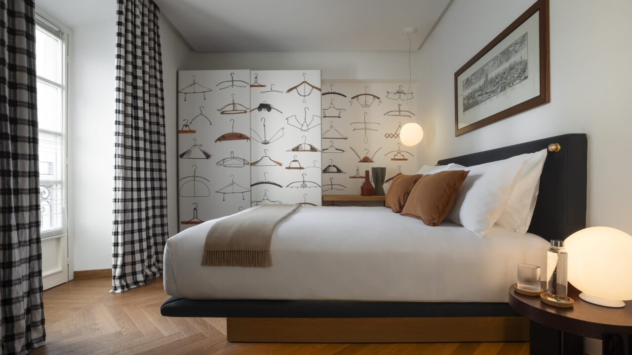 A well-lit modern bedroom featuring a bed with white and brown bedding, a nightstand, and a window with plaid curtains.