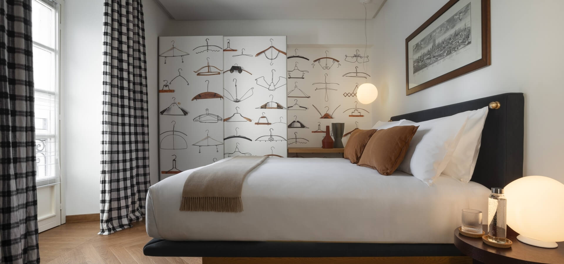 Cozy bedroom with a black upholstered bed, nightstand, globe lamp, and wallpaper featuring colorful hangers.