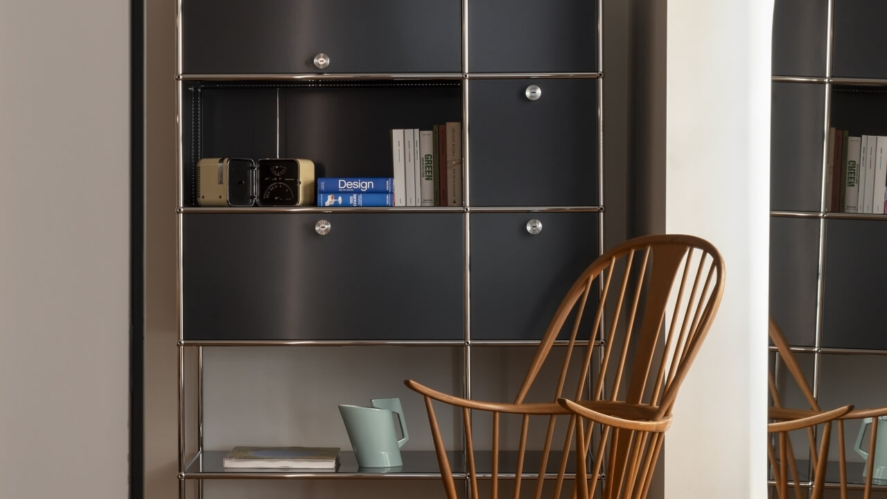 Modern minimalist interior with a metal shelving unit, books, and a wooden chair beside a light blue pitcher.