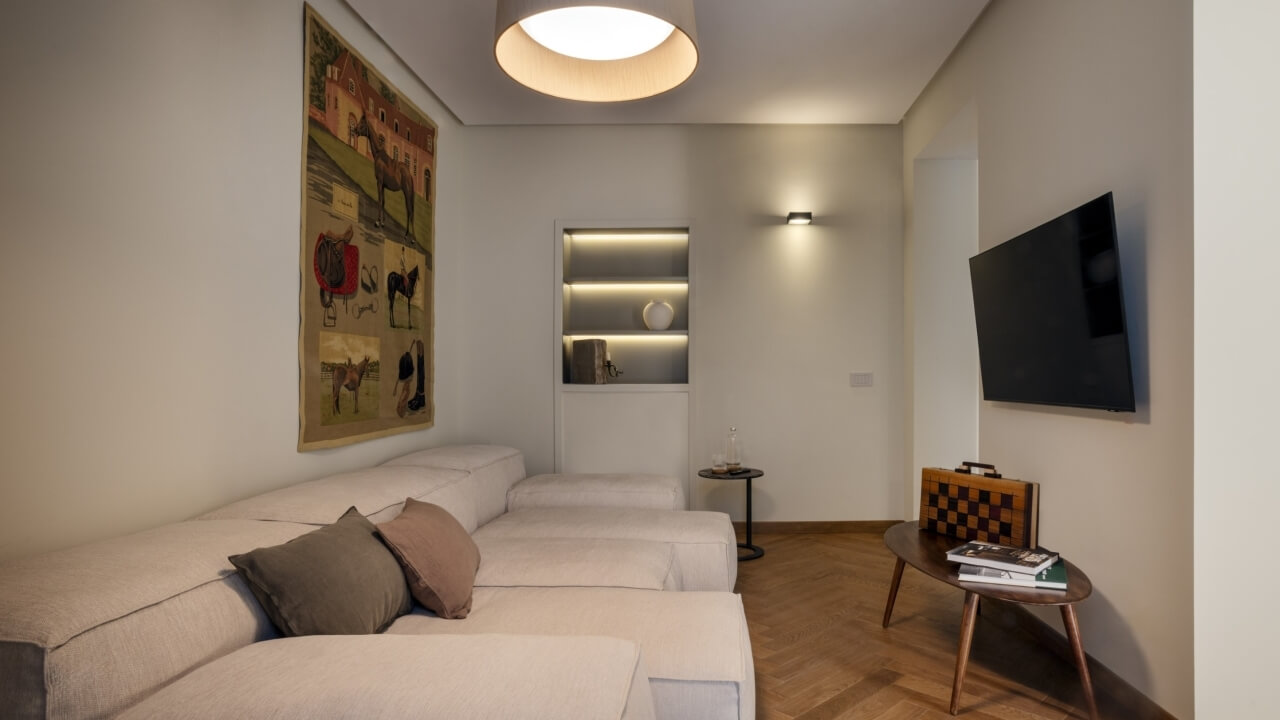 Living room with a white couch, large animal painting, TV, wooden herringbone floor, and elegant lighting.