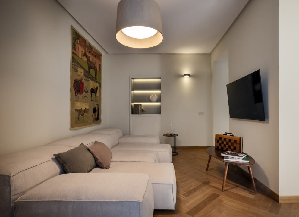 Soggiorno luminoso con divano bianco, arazzo colorato, TV montata e decorazioni accoglienti.