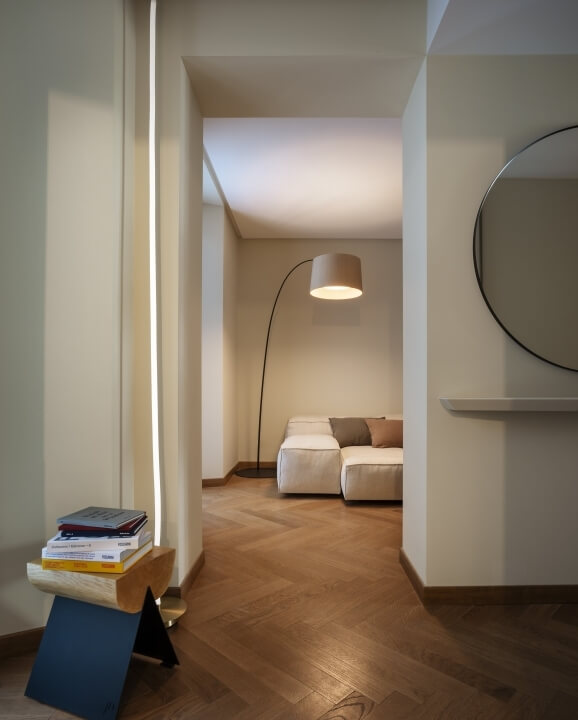 Un soggiorno moderno e sereno con un tavolo in legno, specchio circolare, divano bianco e lampada da terra nera.