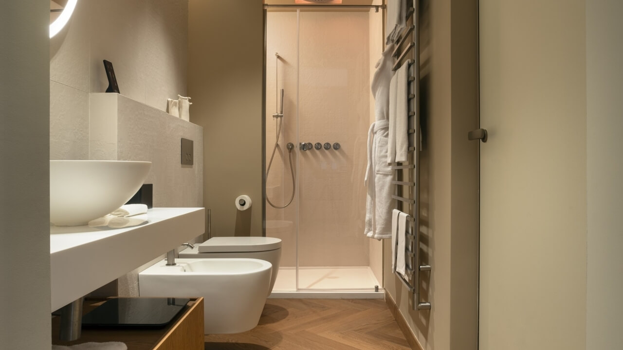 Contemporary bathroom with sink, toilet, walk-in shower, beige tiles, wooden herringbone floor, and mirrored cabinet.