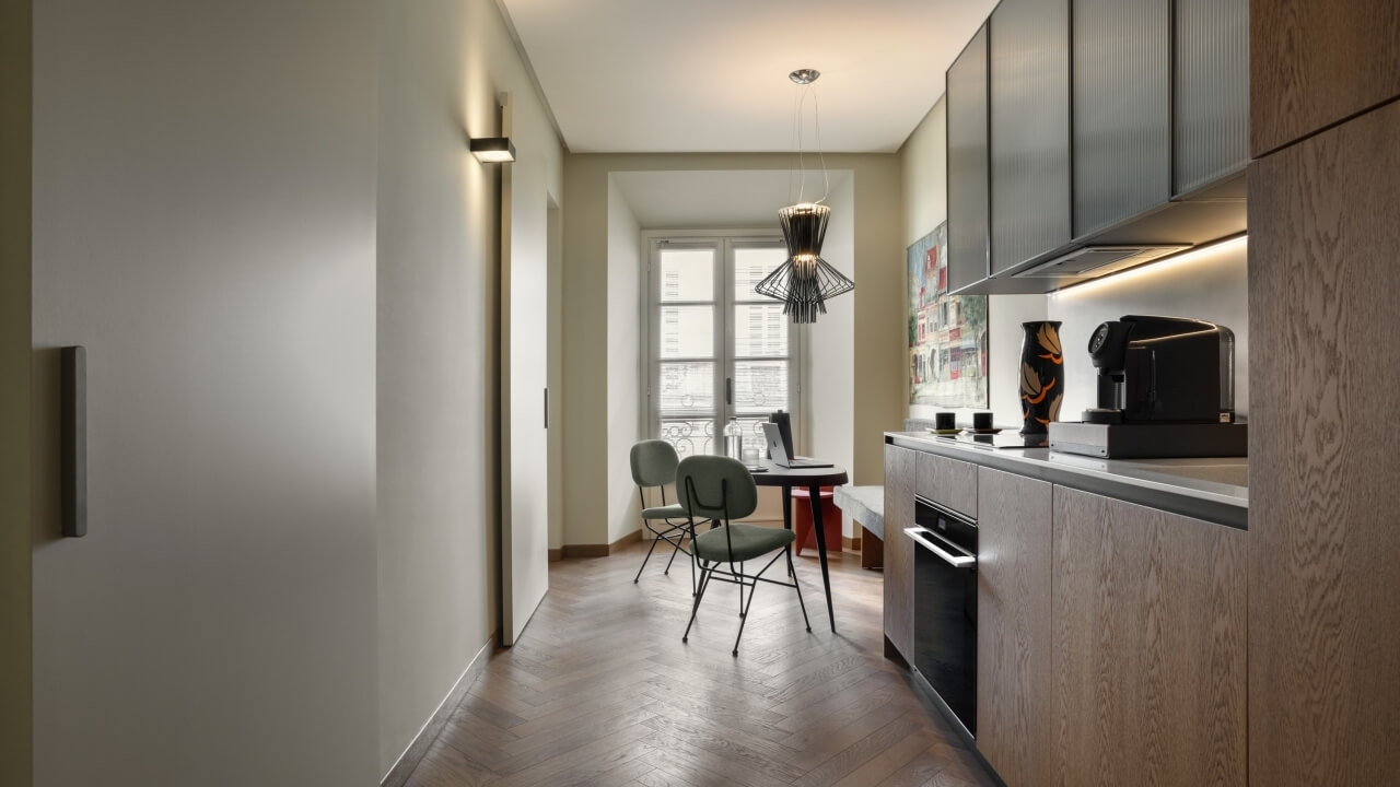 Modern kitchen-living space with beige walls, black cabinets, white countertops, and natural light from a large window.