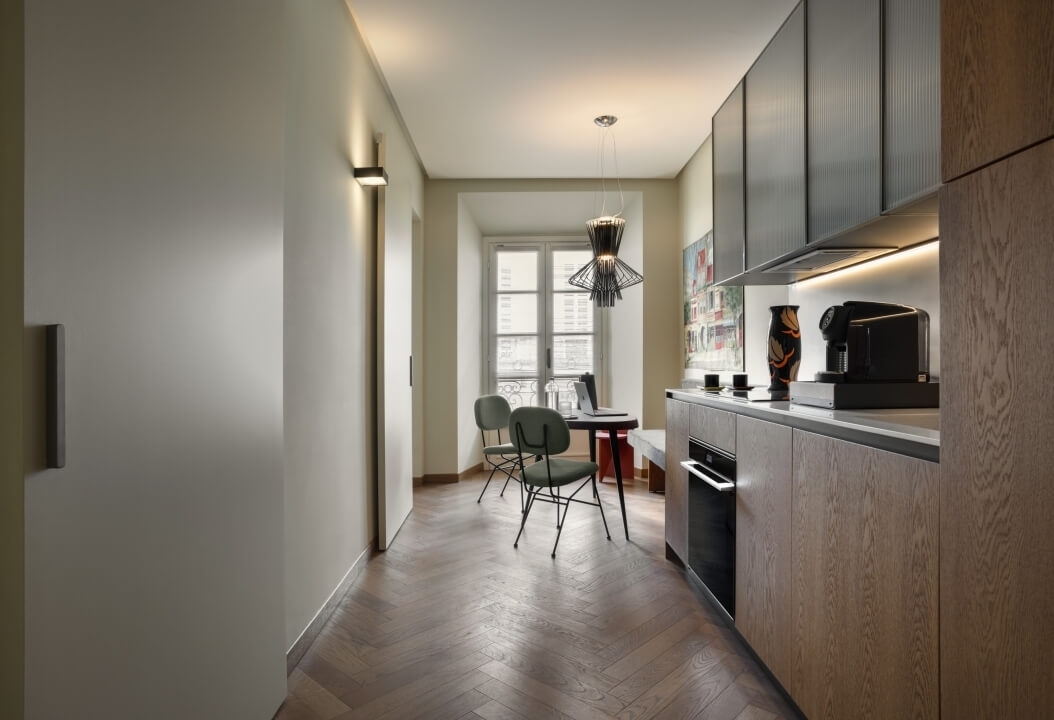 Cucina moderna con area pranzo, armadietti in legno, elettrodomestici in acciaio inox e due sedie verdi attorno a un tavolo.