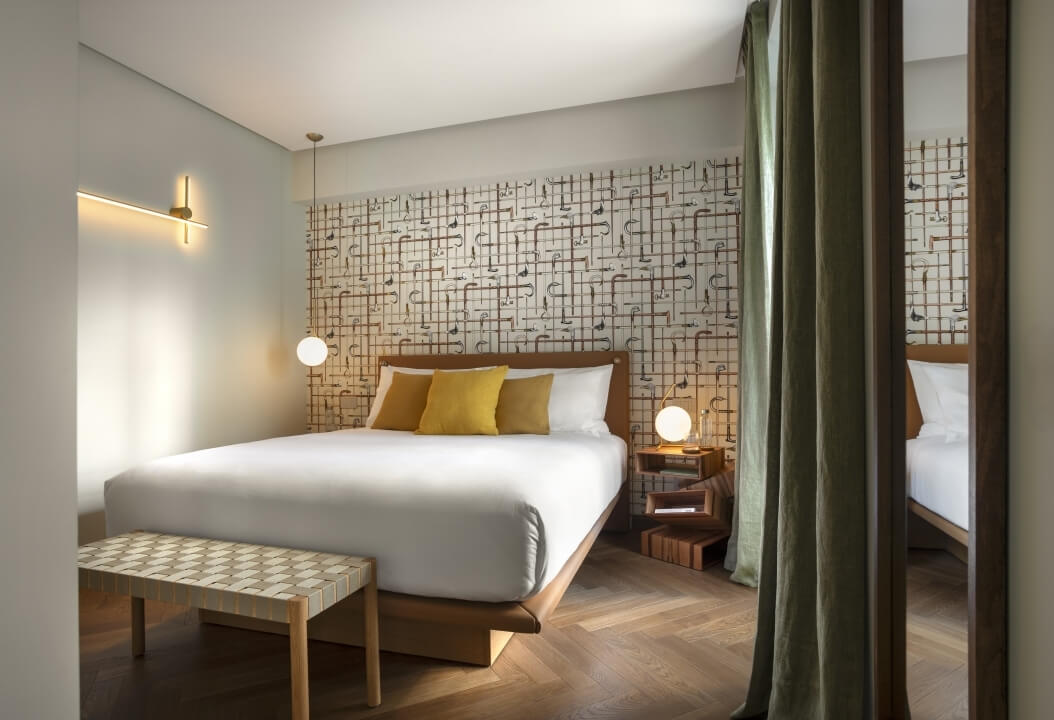 Camera d'albergo serena con tonalità terrose, letto in legno, lampade sospese e decorazioni accoglienti.