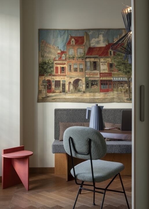 Una stanza accogliente con un dipinto di una scena di strada europea, panchina grigia con cuscini e sedia blu.